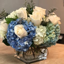 Blue and white hydrangeas with cream roses in a square glass vase