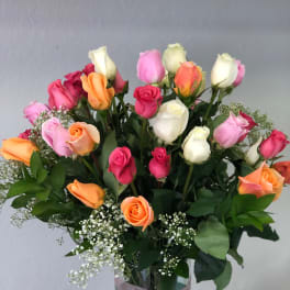 Mixed roses in pink, white, and orange arranged in a glass vase with a pink ribbon