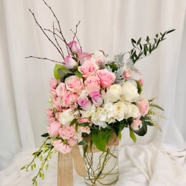 Pink and white rose arrangement in a clear glass vase with ribbon