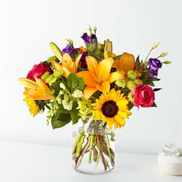 Mixed bouquet of lilies, roses, and a sunflower in a clear glass vase