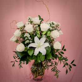 White roses and a white lily in a glass vase with small daisy flowers
