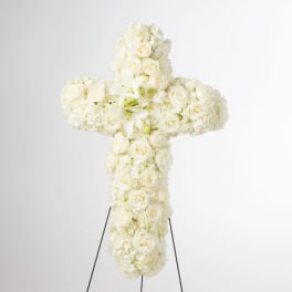 White floral cross on a stand with roses and hydrangeas
