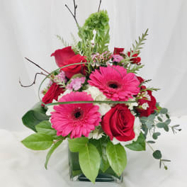 Pink gerbera daisies and red roses arranged in a glass vase