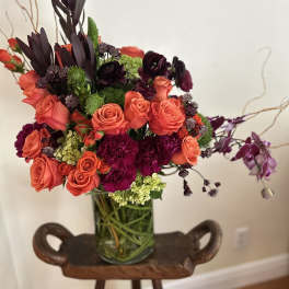 Coral roses and dark purple flowers arranged in a glass vase