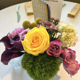Mixed floral centerpiece with a yellow rose, purple calla lilies, and pink roses