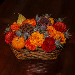 Basket arrangement with orange and red flowers, pumpkins, and thistle-like accents
