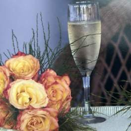 Yellow and pink roses arranged beside a champagne flute