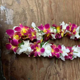 Two floral leis made of pink, yellow, and white orchids on a wooden surface