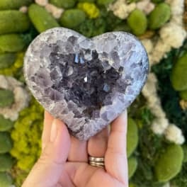 Hand holding a heart-shaped crystal stone in front of a floral wall