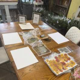 Craft supplies and framed floral pieces arranged on a wooden table