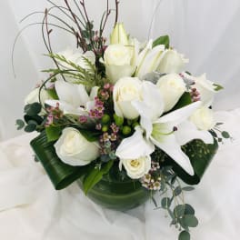 White roses and lilies arranged in a low vase with greenery