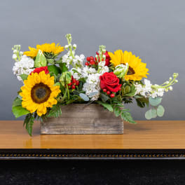 Sunflowers and red roses in a wooden box with white blooms