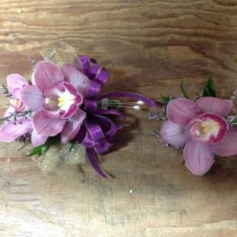 Two pink orchid corsages with purple ribbon on a wooden surface
