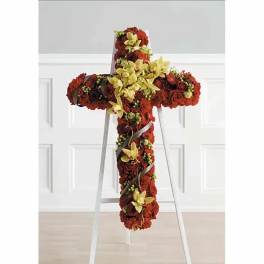 Cross-shaped floral tribute with red flowers and yellow orchids on a stand