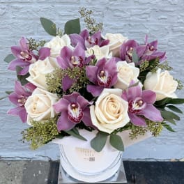 White roses and purple orchids arranged in a round white box