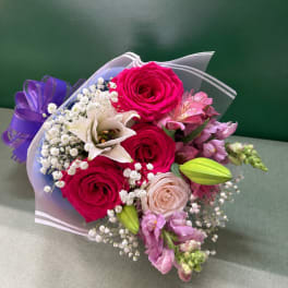 Bouquet of pink roses, white lily, and purple flowers wrapped in clear paper