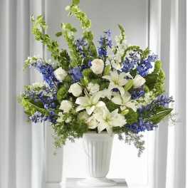 White lilies and blue flowers arranged in a white pedestal vase