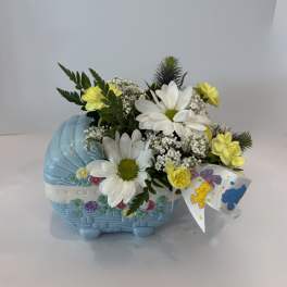 Yellow and white flowers arranged in a blue basket with a teddy bear ribbon