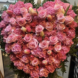 Heart-shaped pink floral arrangement with roses and carnations on an easel