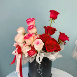Red and blush roses arranged in a black hat box with ribbon