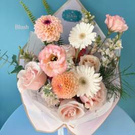 Blush bouquet with roses, gerbera daisies, and peach blooms in white wrap