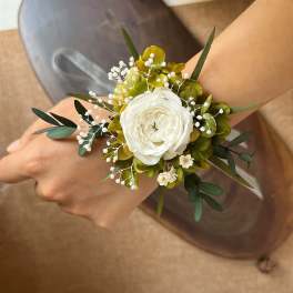White floral wrist corsage with green foliage and small white filler flowers