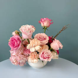 Pink roses and carnations arranged in a white bowl vase