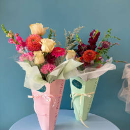 Two wrapped bouquets with pink, cream, and orange flowers in pastel boxes