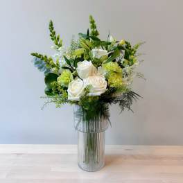 White roses and green flowers in a tall ribbed glass vase