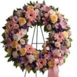 Large pastel floral wreath on a metal stand with pink ribbon