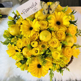 Round yellow flower basket with gerbera daisies, roses, lemons, and a name card topped with a butterfly.