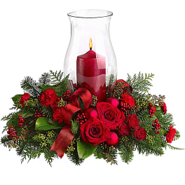 Red roses and carnations around a lit candle in a glass hurricane vase