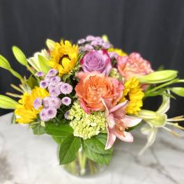 Mixed bouquet of roses, lilies, and sunflowers in a glass vase