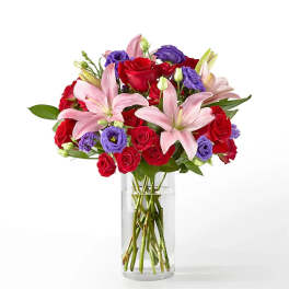 Bouquet of red roses, pink lilies, and purple blooms in a clear glass vase