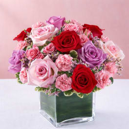 Bouquet of pink, red, and lavender roses in a square glass vase