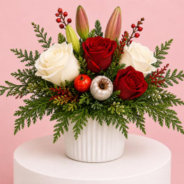 Red and white roses in a white vase with evergreen accents and berries