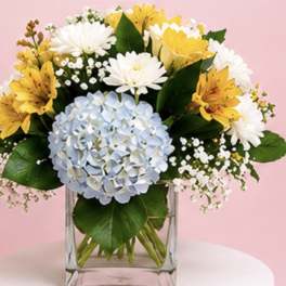 Bouquet of yellow and white flowers with a blue hydrangea in a clear glass vase