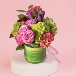 Pink and purple bouquet in a glass vase with a pink ribbon