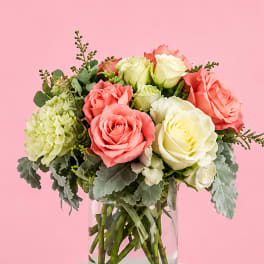 Pink and white roses in a clear glass vase with green filler flowers