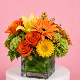 Orange and yellow flowers arranged in a clear square vase