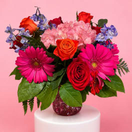 Mixed bouquet of roses, hydrangea, and gerbera daisies in a glass vase