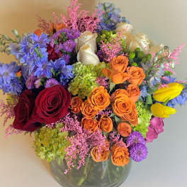 Mixed bouquet of roses, hydrangeas, and blue flowers in a glass vase