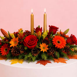 Autumn floral centerpiece with red roses, orange daisies, and two gold candles
