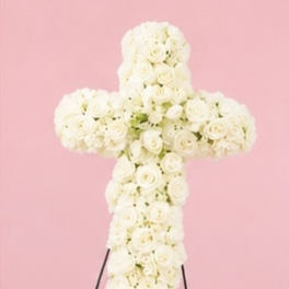 White rose cross-shaped floral arrangement on a stand against a pink background