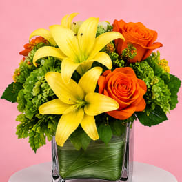 Yellow lilies and orange roses in a clear square vase