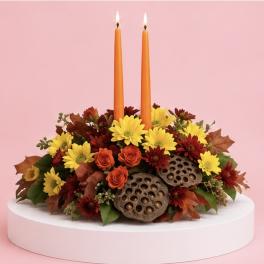 Autumn floral centerpiece with two orange taper candles on a white pedestal