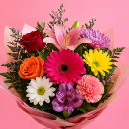 Mixed bouquet with roses, lilies, daisies, and a pink ribbon wrap