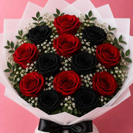 Bouquet of red and black roses with small white filler flowers, wrapped in white paper and tied with a black ribbon.