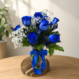 Blue roses and white baby's breath in a glass vase with a blue ribbon