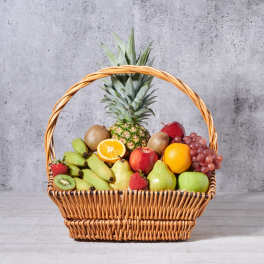 Wicker basket filled with assorted fruit including pineapple, grapes, apples, pears, bananas, and kiwi